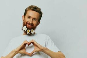 Portrait of a funny man in a white T-shirt with flowers daisies in his beard on a white isolated background, copy place. Holiday concept and congratulations. photo