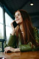 mujer con rojo pelo Lanza libre blogger sentado en un café hablando en el teléfono y sonriente, hipster niña en de moda ropa estilo de vida foto