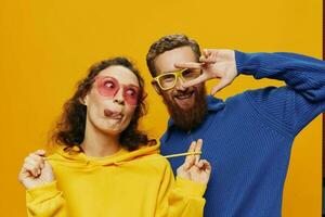 Man and woman couple smiling cheerfully and crooked with glasses, on yellow background, symbols signs and hand gestures, family shoot, newlyweds. photo