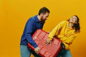 Woman and man smiling, suitcases in hand with yellow and red suitcase smiling merrily and crooked, yellow background, going on a trip, family vacation trip, newlyweds. photo