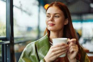 Portrait of a woman influencer drinking a drink from a mug in a cafe and smiling looking out the window, content blogger close-up photo