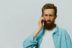 hombre hipster con teléfono en mano blogger sonrisa en gris antecedentes en azul camisa y blanco camiseta, hablando en el teléfono y selfies foto