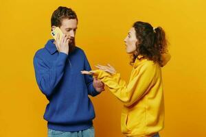 Man and woman couple with phone in hand call talking on the phone, on a yellow background, symbols signs and hand gestures, family quarrel jealousy and scandal. photo