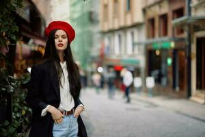 mujer Moda modelo soportes en el calle en el ciudad entre el multitud en un chaqueta y rojo boina y vaqueros, cinematográfico francés Moda estilo ropa, viaje a Estanbul foto