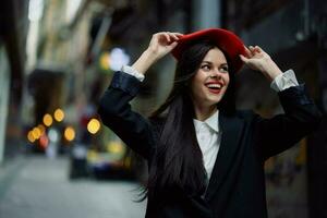 Moda mujer sonrisa con dientes y divertido turista en elegante ropa en chaqueta y rojo boina caminando abajo estrecho ciudad calle volador cabello, viajar, francés estilo, cinematográfico color, retro Clásico estilo. foto