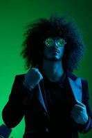 Fashion portrait of a man with curly hair on a green background with sunglasses, multinational, colored pink light, trendy, modern concept. photo