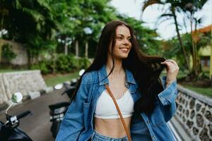 Portrait of woman brunette smile with teeth running down the street against backdrop palm trees in the tropics, summer vacations and outdoor recreation, the carefree lifestyle of a freelance student. photo