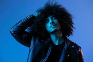 Portrait of fashion man with curly hair on blue background multinational, colored light, black leather jacket trend, modern concept. photo