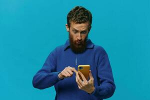 Portrait of a man with a phone in his hands does looking at it and talking on the phone, on a blue background. Communicating online social media, lifestyle photo