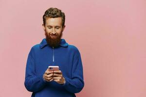Portrait of a man with a phone in his hands doing looking at it and talking on the phone, on a pink background. Communicating online social media, lifestyle photo