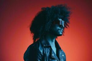 Portrait of fashion man with curly hair on red background with stylish glasses, multicultural, colored light, black leather jacket trend, modern concept. photo