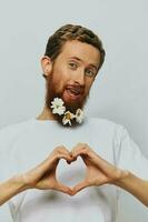 Portrait of a funny man in a white T-shirt with flowers daisies in his beard on a white isolated background, copy place. Holiday concept and congratulations. photo