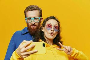 Woman and man funny couple with phones hand social networking and communication crooked do selfies smile fun, on yellow background. The concept of real family relationships, freelancers, work online. photo