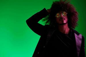 Fashion portrait of a man with curly hair on a green background with sunglasses, multinational, colored pink light, trendy, modern concept. photo