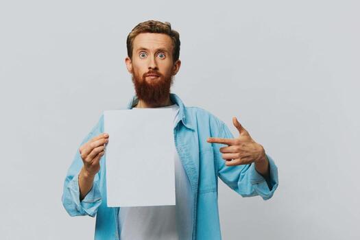 Portrait of an adult male on a gray background with a white sheet of paper in his hands for your design and text, layout, copy space, space for text, finger pointing photo