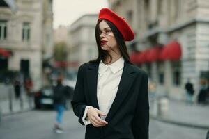 Moda mujer retrato sonrisa con dientes en pie en el calle en el ciudad antecedentes en elegante ropa rojo labios y rojo boina, viajar, cinematográfico color, retro Clásico estilo, urbano Moda estilo de vida. foto