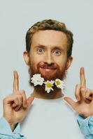 retrato de un gracioso hombre en un blanco camiseta con flores margaritas en su barba en un blanco aislado fondo, Copiar lugar. fiesta concepto y Felicidades. foto