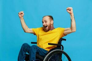 un hombre en un silla de ruedas felicidad elevado su manos arriba en un camiseta con tatuajes en su manos se sienta en un azul estudio fondo, un lleno vida, un real persona foto