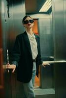 elegante mujer en negro chaqueta y Gafas de sol posando en ascensor, Moda modelo, oscuro cinematográfico ligero y color foto