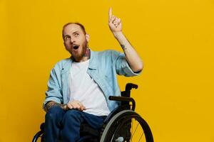 A man in a wheelchair surprised, with tattoos on his arms sits on a yellow studio background, the concept of health is a person with disabilities photo