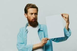 Portrait of an adult male on a gray background with a white sheet of paper in his hands for your design and text, layout, copy space, space for text, finger pointing photo