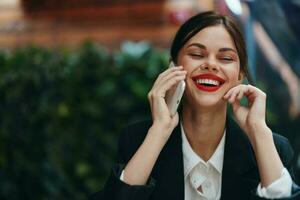 Woman blogger tourist sits in a cafe at a table with a phone in her hands conversation, mobile communication and internet in spring travel, video business call, freelance work online, smile with teeth photo