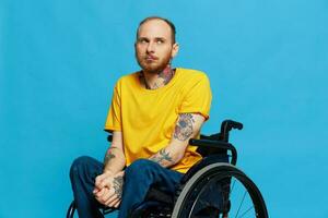 un hombre se sienta en un silla de ruedas en un camiseta en un azul antecedentes en el estudio, el concepto de un gratis sin barreras ambiente para personas con discapacidades foto