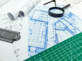 Architect rolls, compass, magnifier glass and house plans, close up. Side view photo