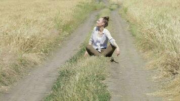 giovane signora seduta nel il mezzo di il strada su il Grano campo video