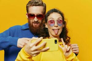 Woman and man funny couple with phones hand social networking and communication crooked do selfies smile fun, on yellow background. The concept of real family relationships, freelancers, work online. photo