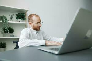 un hombre silla de ruedas empresario en el oficina trabajos a un computadora portátil, escritura abajo ideas y un plan en un computadora portátil, consideración, integración dentro sociedad, el concepto de trabajando un persona con discapacidades foto