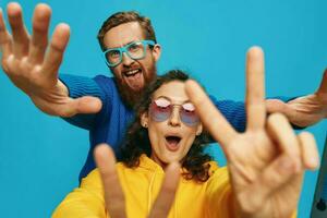 un mujer y un hombre divertido Pareja arrancando y demostración señales con su manos sonriente alegremente, en un azul fondo, el concepto de un real relación en un familia. foto