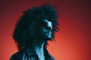 Portrait of fashion man with curly hair on red background with stylish glasses, multicultural, colored light, black leather jacket trend, modern concept. photo