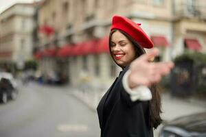 Moda mujer sonrisa con dientes en pie en el calle en frente de el ciudad turista seguir yo elegante ropa con rojo labios y rojo boina, viajar, cinematográfico color, retro Clásico estilo, urbano moda. foto