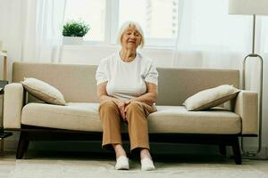 Elderly woman severe abdominal pain sitting on the sofa, health problems in old age, poor quality of life. Grandmother with gray hair holding her stomach, poisoning, problems with stool. photo