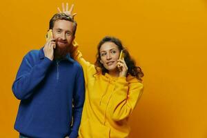 mujer y hombre alegre Pareja con Los telefonos en mano hablando en célula teléfono torcido sonrisa alegre, en amarillo antecedentes. el concepto de real familia relaciones, hablando en el teléfono, trabajo en línea. foto