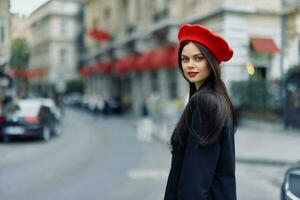 Moda mujer retrato belleza en pie en el calle en frente de el ciudad en elegante ropa con rojo labios y rojo boina, viajar, cinematográfico color, retro Clásico estilo, urbano Moda estilo de vida. foto