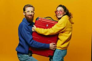 Woman and man smiling, suitcases in hand with yellow and red suitcase smiling merrily and crooked, yellow background, going on a trip, family vacation trip, newlyweds. photo