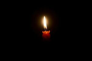 A single burning candle flame or light glowing on an orange candle on black or dark background on table in church for Christmas, funeral or memorial service with copy space. photo