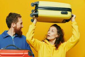Woman and man smiling, suitcases in hand with yellow and red suitcase smiling merrily and crooked, yellow background, going on a trip, family vacation trip, newlyweds. photo