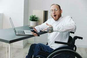 A man in a wheelchair in the office works at a laptop, work online, social networks and startup, copy space, integration into society, concept of health disabled person, real person close-up photo