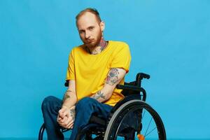 un hombre se sienta en un silla de ruedas en un camiseta en un azul antecedentes en el estudio, el concepto de un gratis sin barreras ambiente para personas con discapacidades foto
