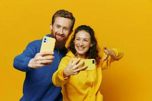 Man and woman couple smiling merrily with phone in hand social media viewing photos and videos, on yellow background, symbols signs and hand gestures, family freelancers.