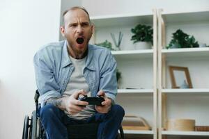 A man in a wheelchair gamer plays games with a joystick in his hands at home, anger and sadness from losing, copy space, with tattoos on his hands, health concept man with disabilities, real person photo