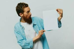 Portrait of an adult male on a gray background with a white sheet of paper in his hands for your design and text, layout, copy space, space for text, finger pointing photo