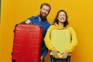 Woman and man smiling, suitcases in hand with yellow and red suitcase smiling merrily and crooked, yellow background, going on a trip, family vacation trip, newlyweds. photo