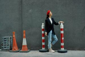 Fashion woman standing leaning against a wall street against a background of the city road works tourist in stylish clothes with red lips and red beret, travel, cinematic color, retro vintage style. photo