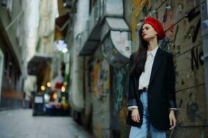Fashion woman portrait walking tourist in stylish clothes with red lips walking down a narrow city street, travel, cinematic color, retro vintage style, dramatic against a wall with graffiti. photo