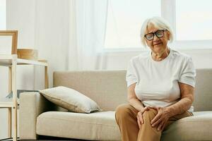 Elderly woman severe pain in her leg sitting on the couch, health problems in old age, poor quality of life. Grandmother with gray hair holds on to her sore knee, problems with joints and ligaments. photo