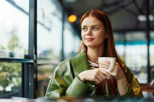 Portrait of a woman influencer drinking a drink from a mug in a cafe and smiling with her teeth looking out the window, content blogger close-up photo